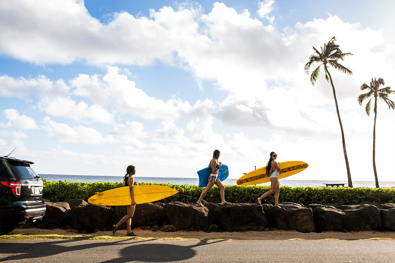 car parked on side of the road with group of friends taking surfboards to the beach