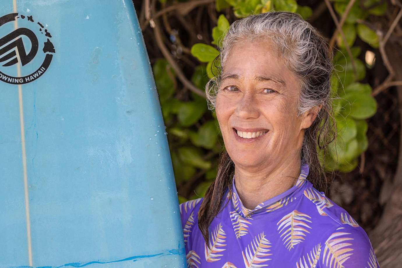 Headshot of Via Podcast guest Mindy Pennybacker next to a surfboard