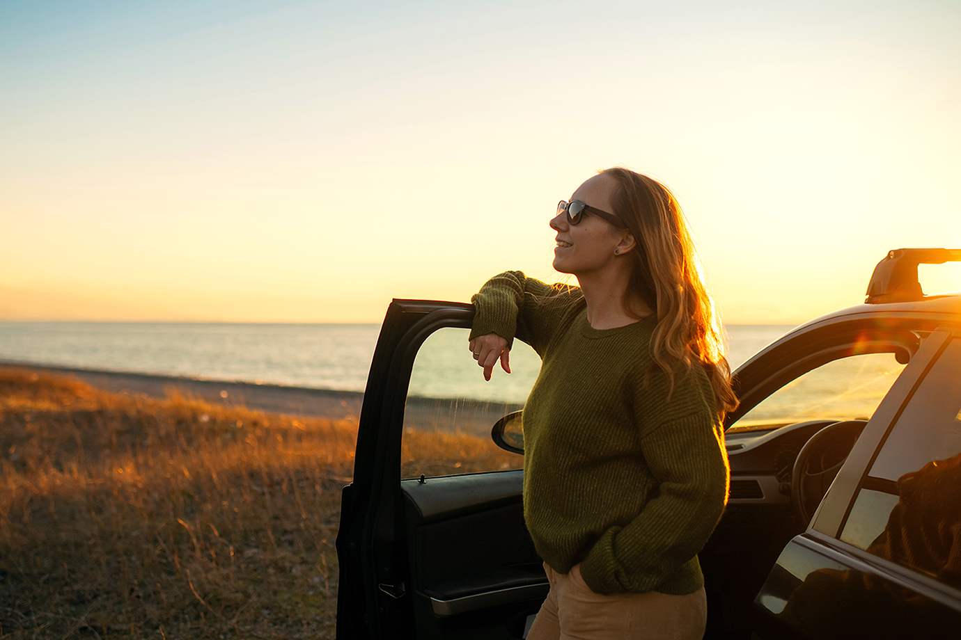 women with sunglasses standing outside the driver's side of a car at sunset