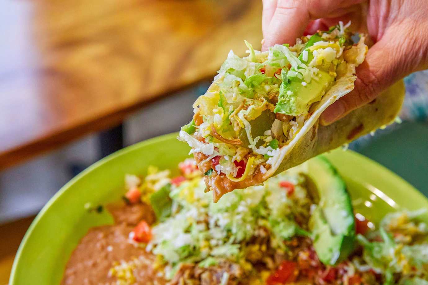 a loaded soft taco held above a taco plate