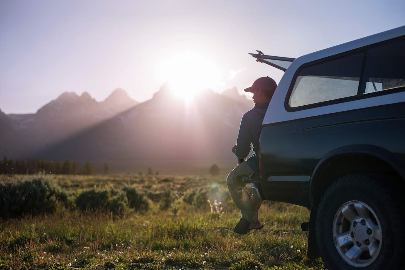 Man sitting in back of pickup truck looking at mountains