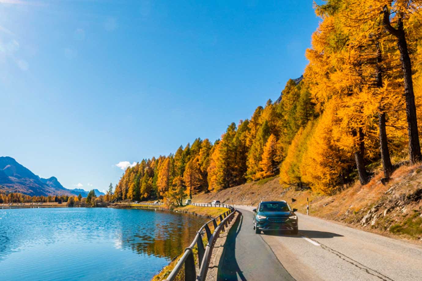 car driving on the road alongside a lake during the fall