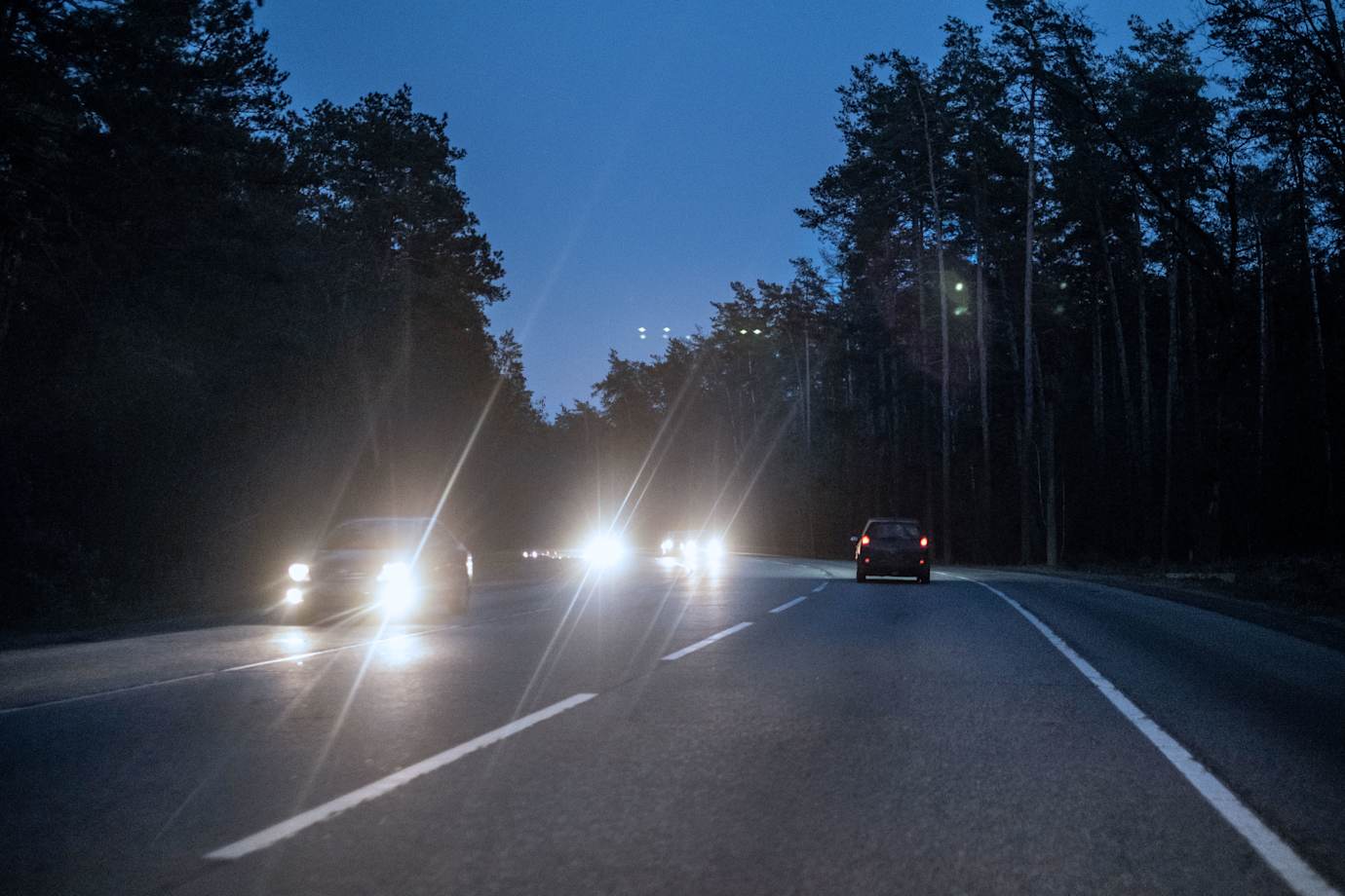 Headlights create glare on a forest highway at night. 