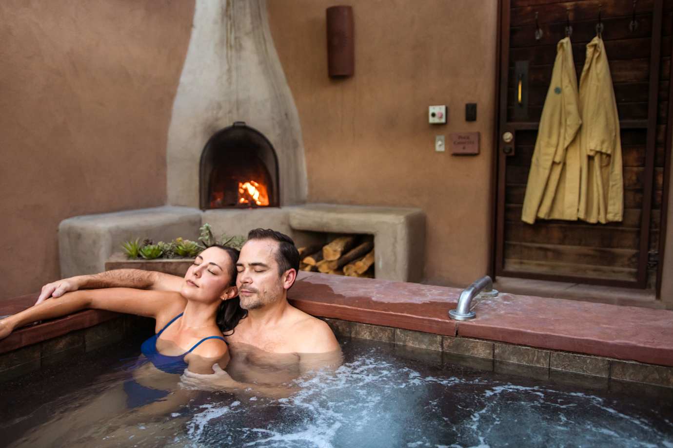 a couple relax in a hot tub in front of a fire at Ojo Santa Fe Spa Resort.