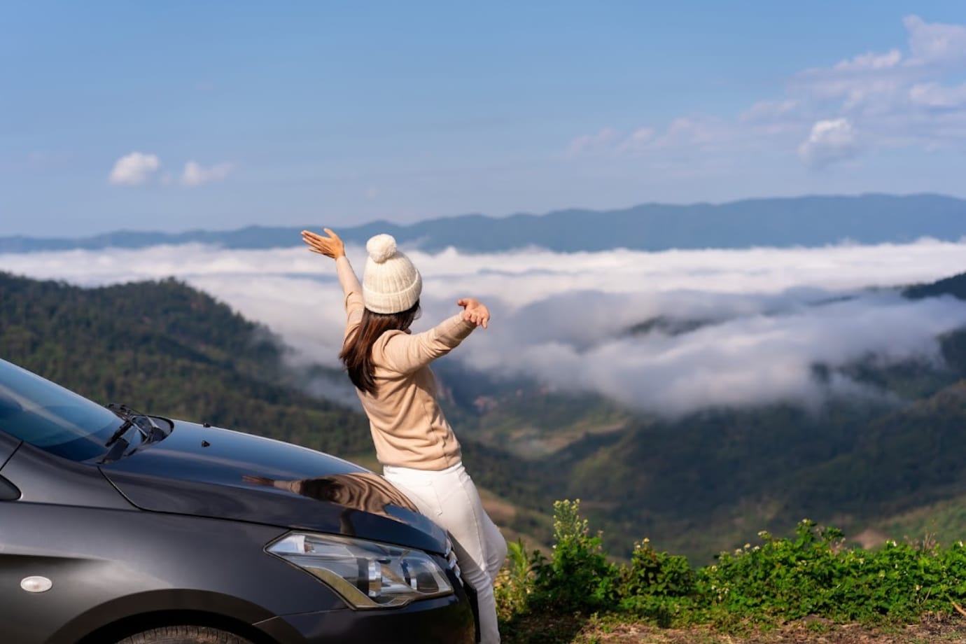 women wearing a beaning sitting on the hood of a car looking out to a valley