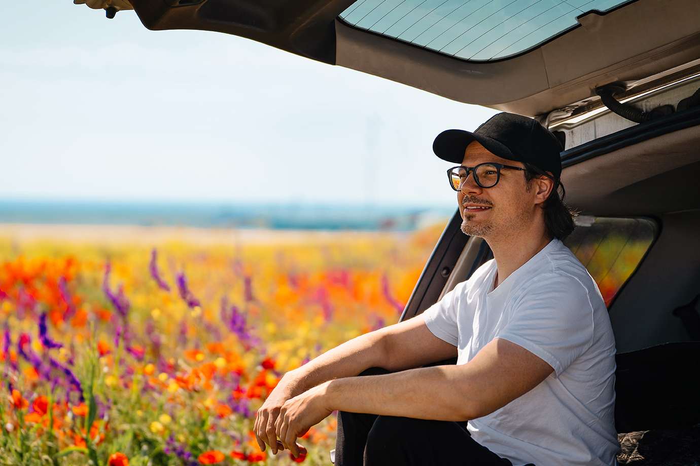 man sitting in the trunk of car in a field of flowers