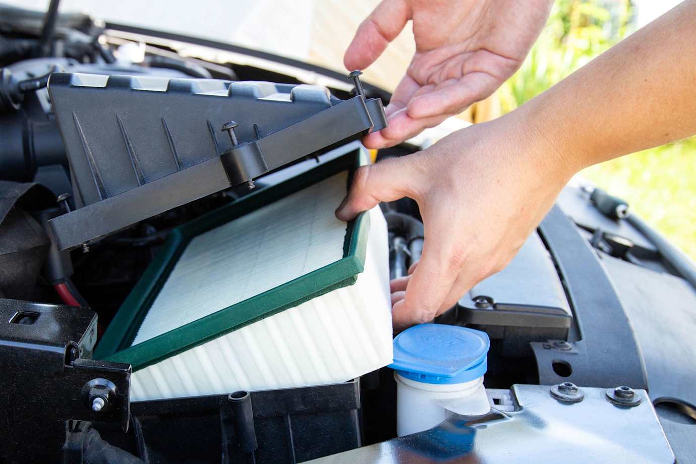 A person replaces their car engine air filter.