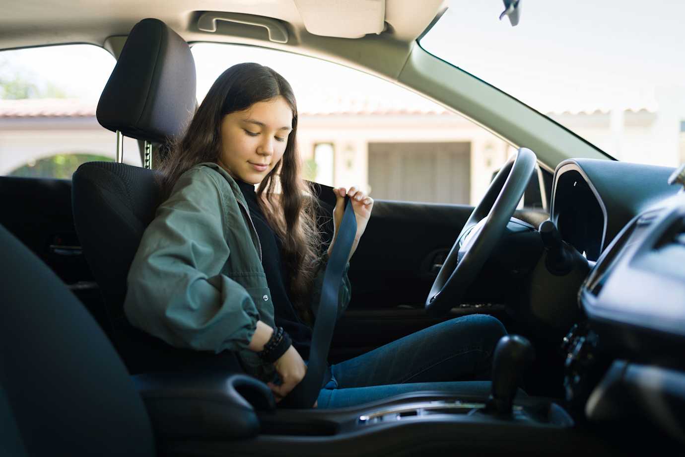 A teen puts on her setbelt before driving on a sunny day.