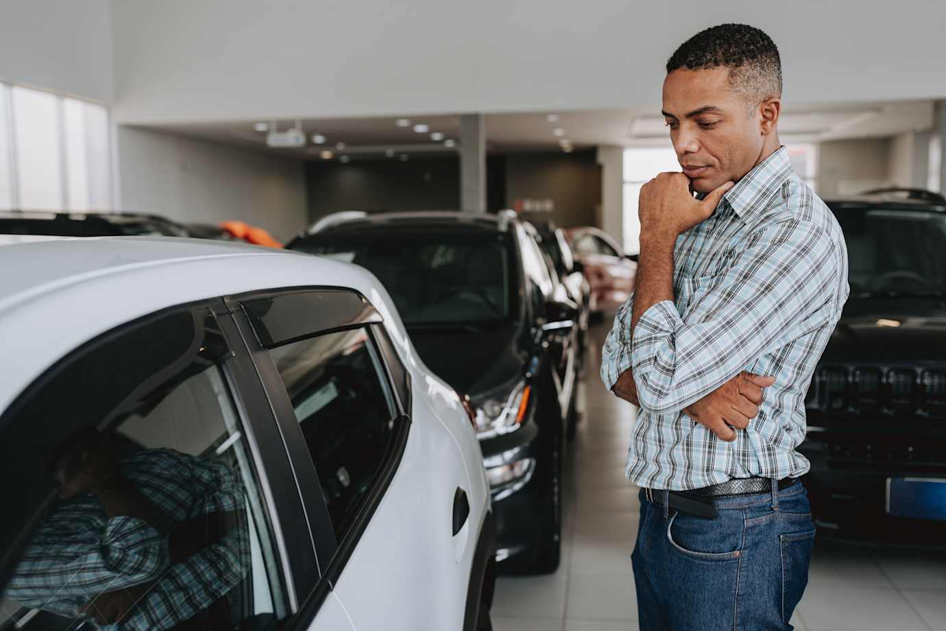 A man looks at a white sedan in a dealership showroom.