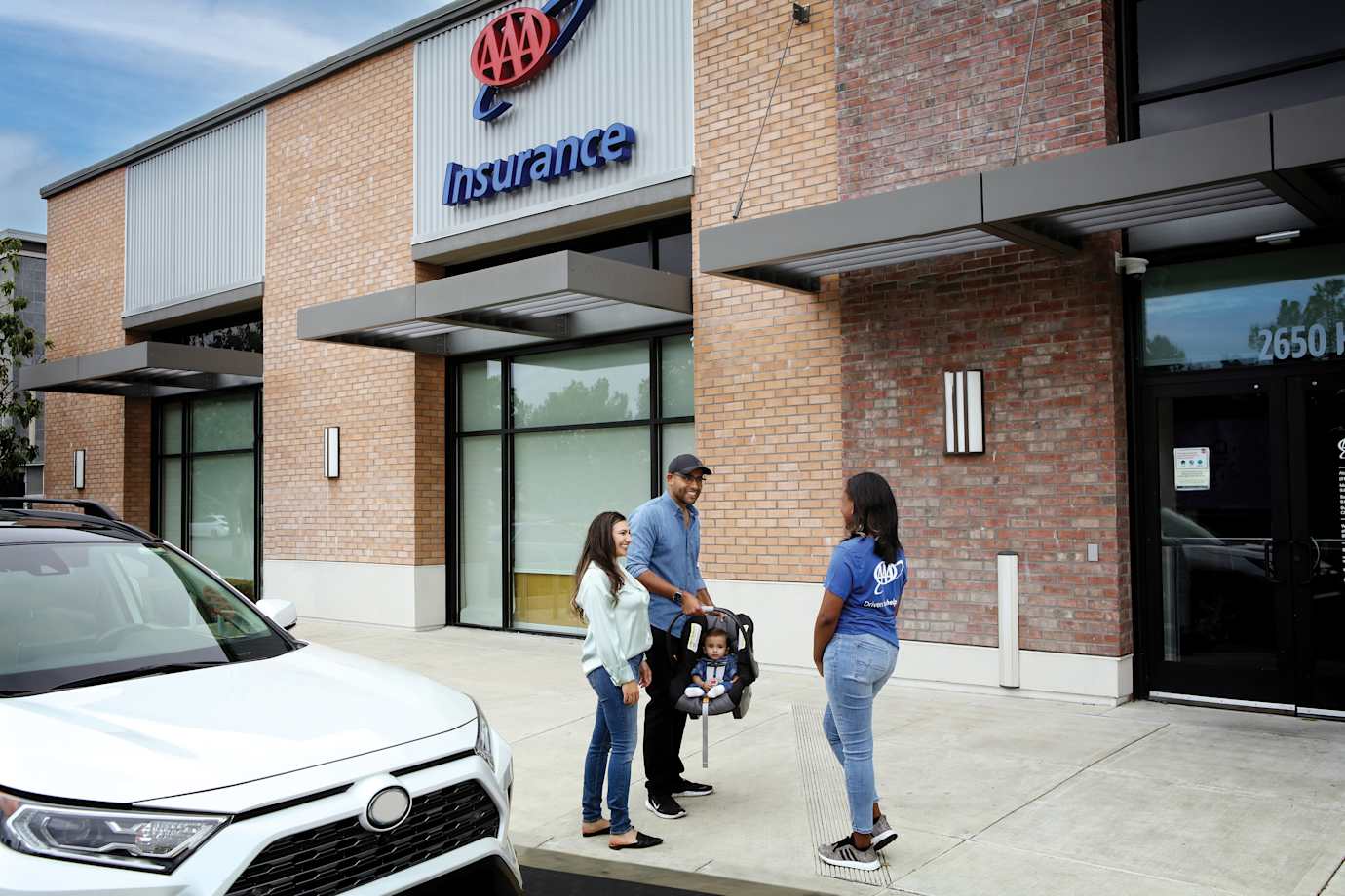 Parents hold their baby in a car seat while talking to a AAA child safety technician.