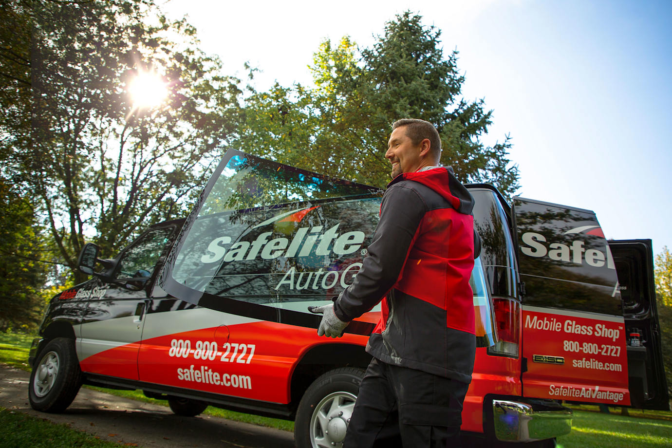 Safelite AutoGlass technician holding a windshield replacement next to his van