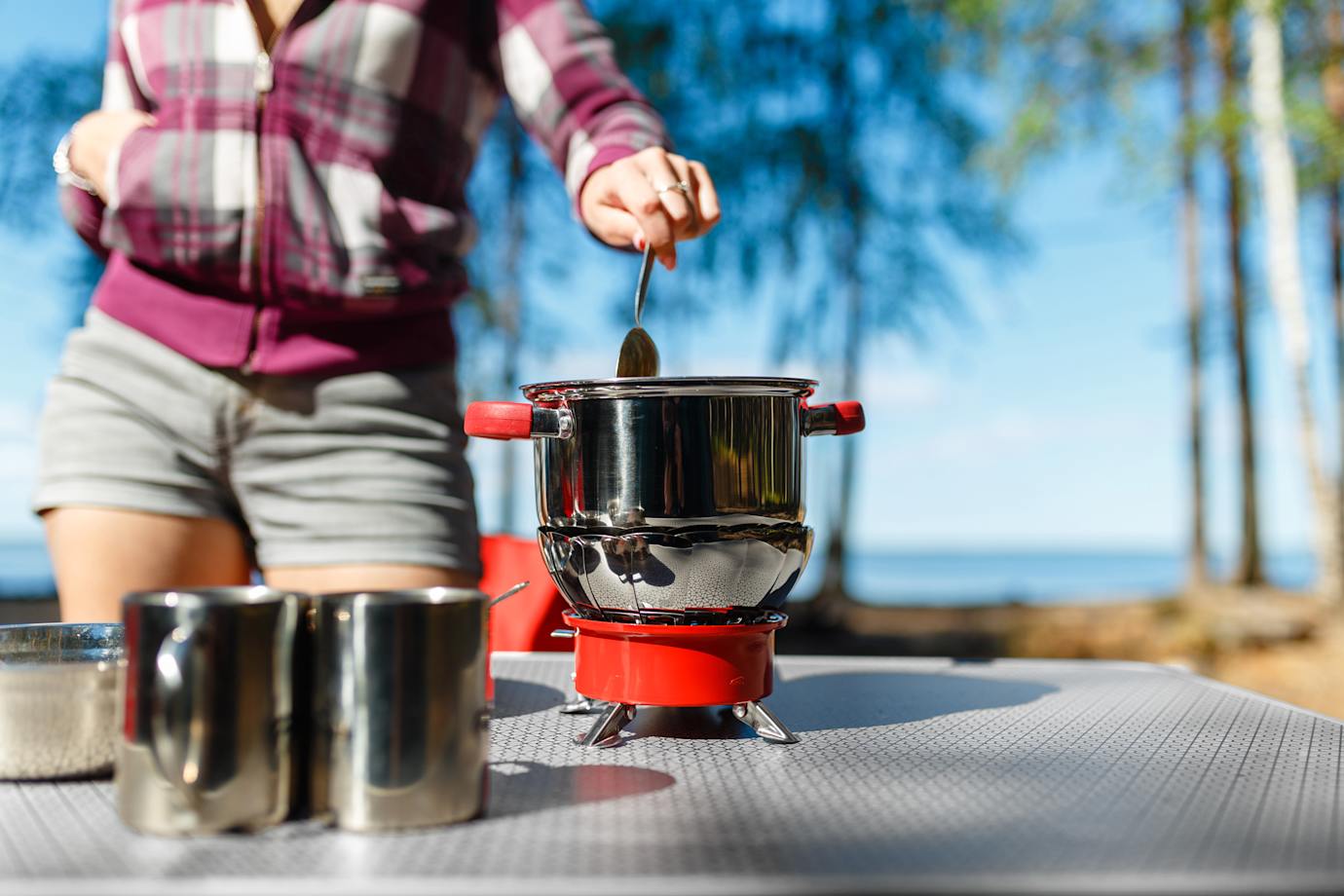 A woman cooks on her camping stove on a picnic table.