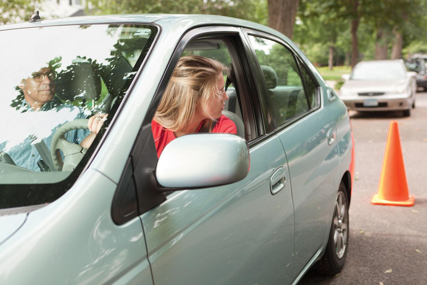 A teen practices reversing a car with her dad in the passenger seat.
