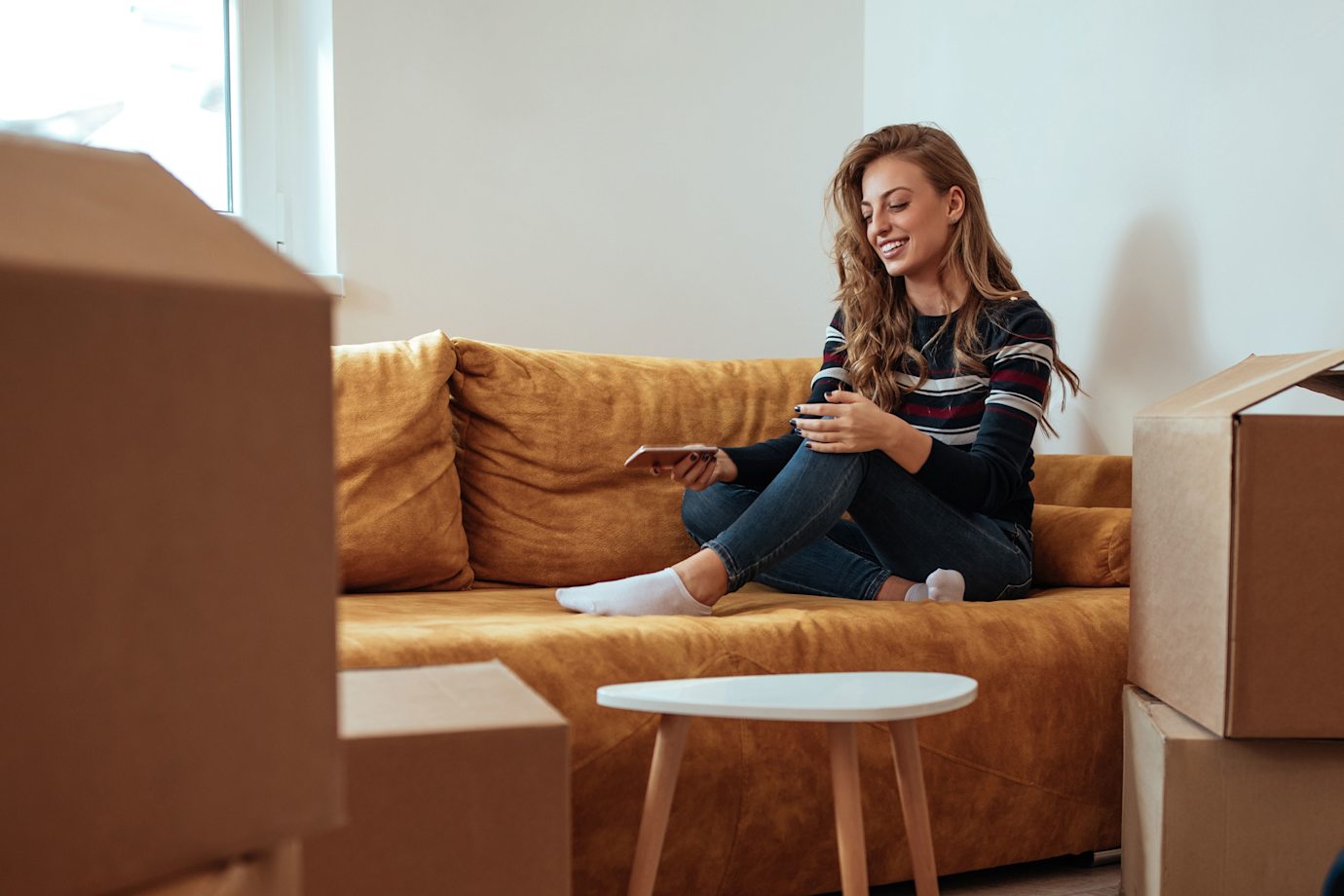 A woman sits on a couch in her new place to compare renters policies