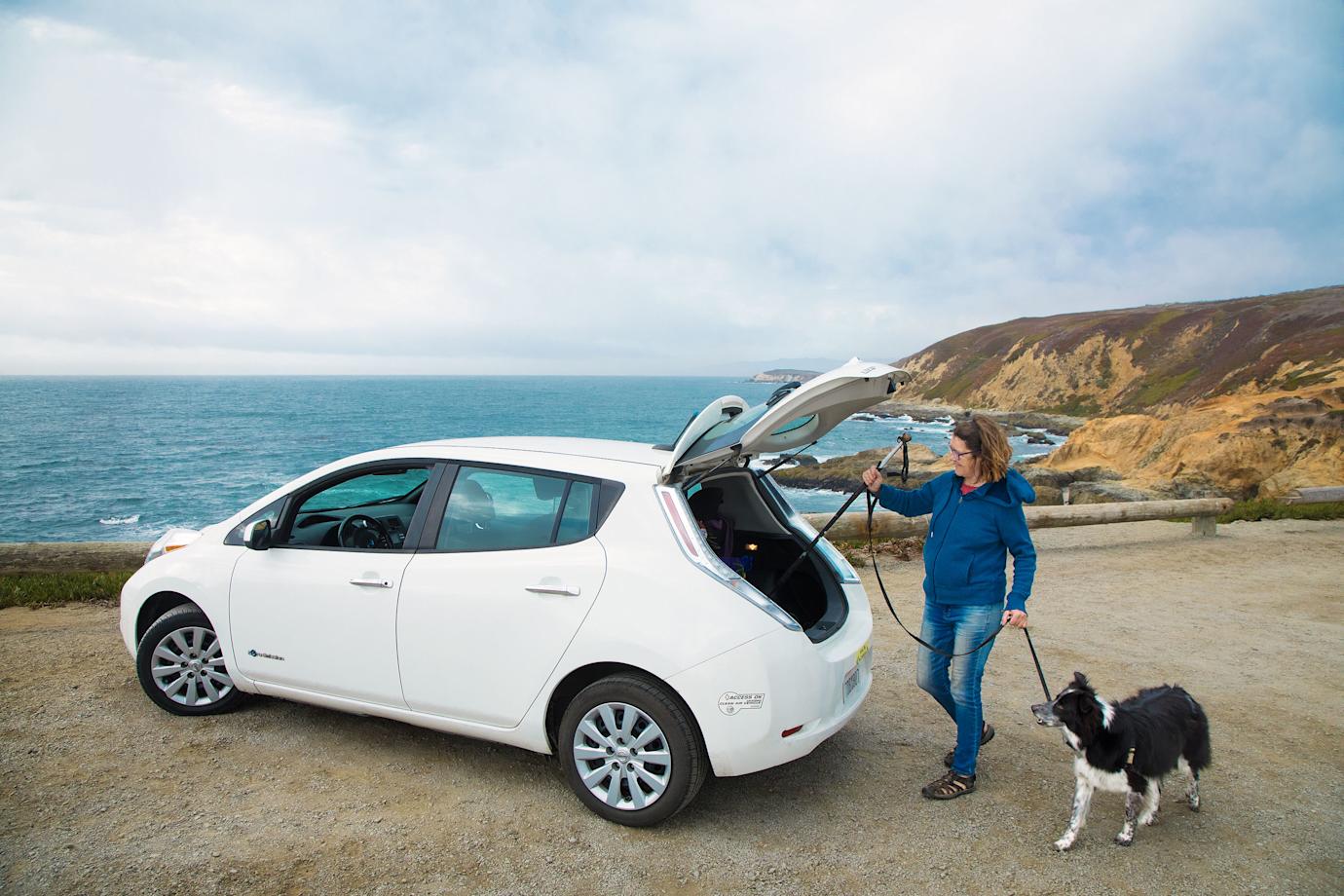 A woman loads hiking poles into the back of her Nissan Leaf EV.