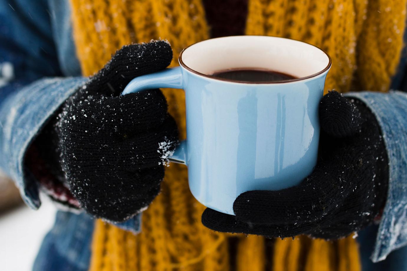 A person holds a blue coffee mug on a snowy morning.