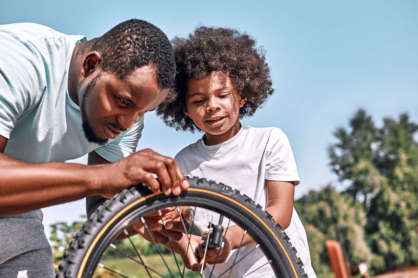 A dad and his son add air to the son's bike tire.