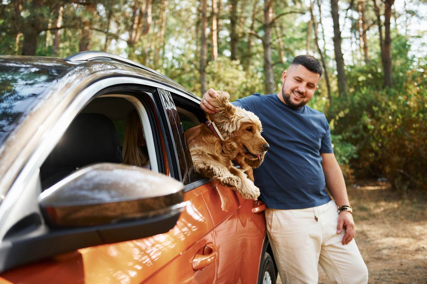 A man stands outside his car and pets his dog in the backseat.