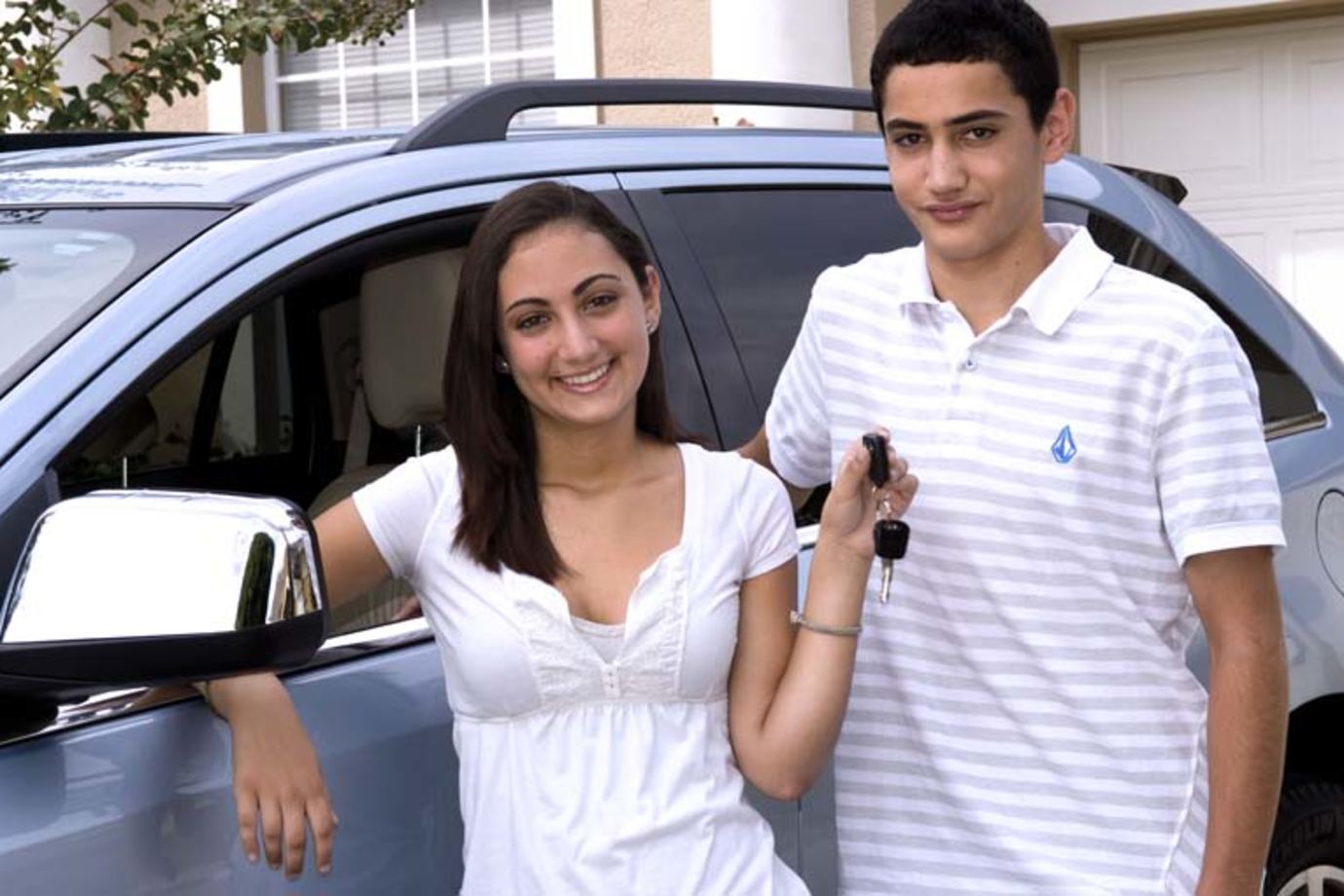 two teenagers in front of a car, the female holds up car keys after successful completion of the driver education course