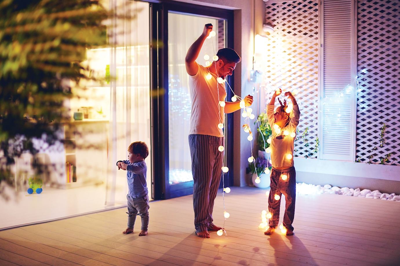 A dad and his two children hang up led string lights on their patio.