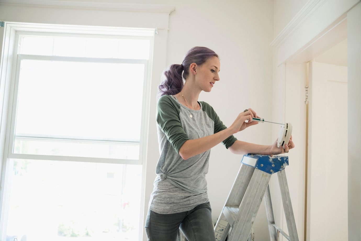 A woman installs a smart smoke alarm in her home.