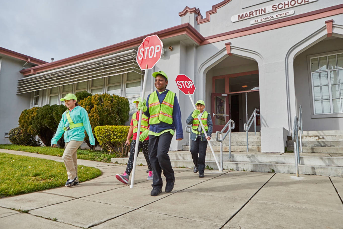 Students who participate in the AAA School Safety Program walk outside of their school with safety vests and stop signs.