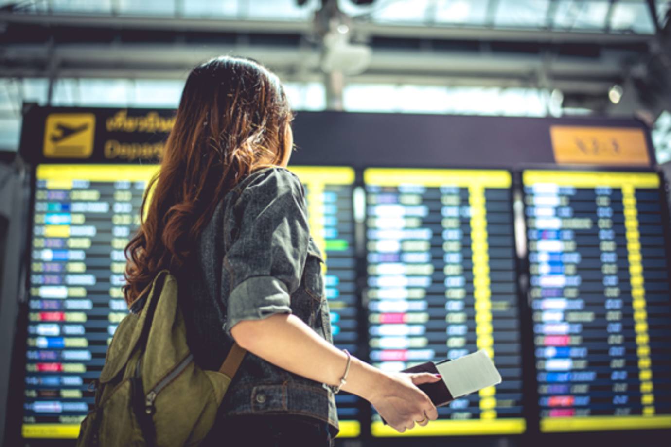 woman with passport at flight status board in airport