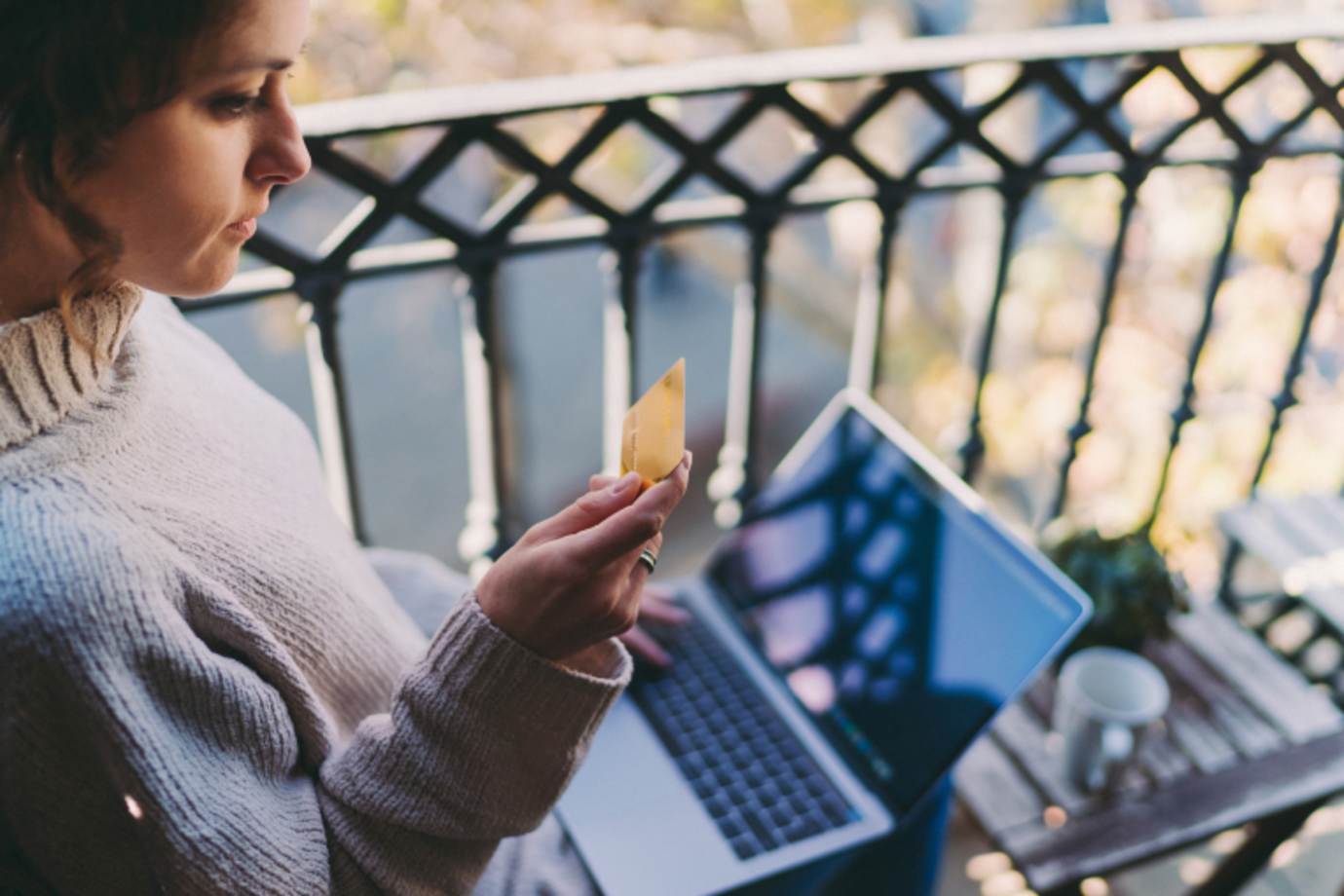 A woman looks at her credit card after getting a fraud alert on her laptop