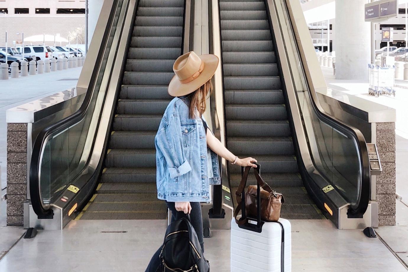 A woman walks through the airport with her white rolling luggage.
