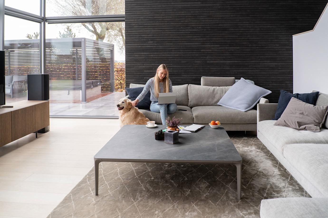 A woman sits on her couch with her dog in a modern home.