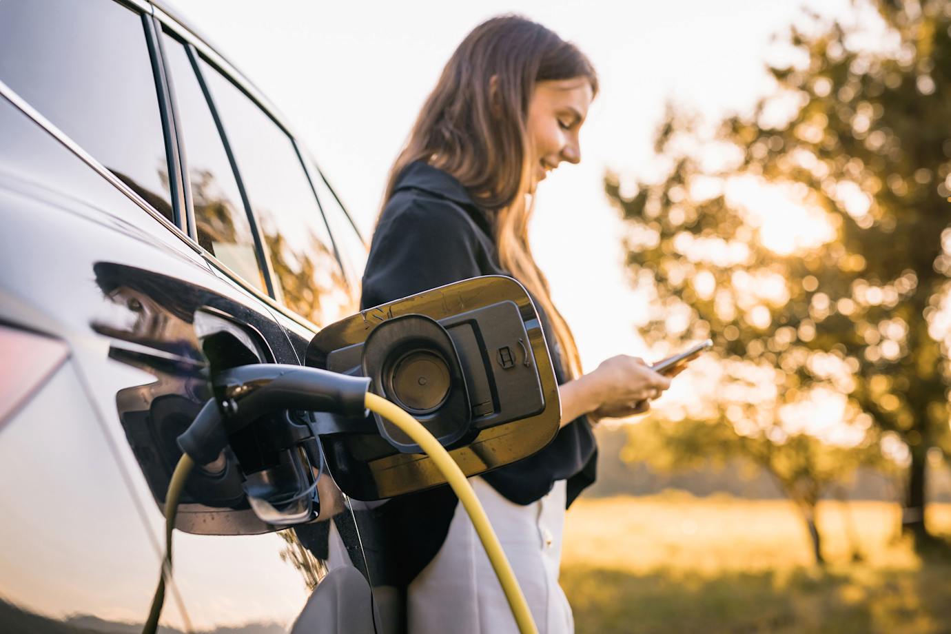 A woman charges her EV on a fall day.