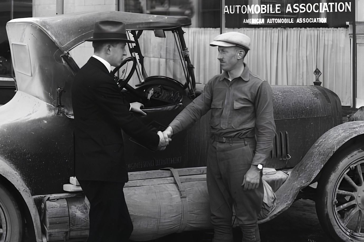 Two men shake hands in a historic black and white photo outside of a AAA office.