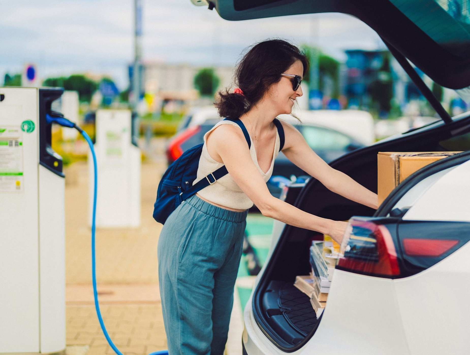 A woman loads the trunk of her charging EV