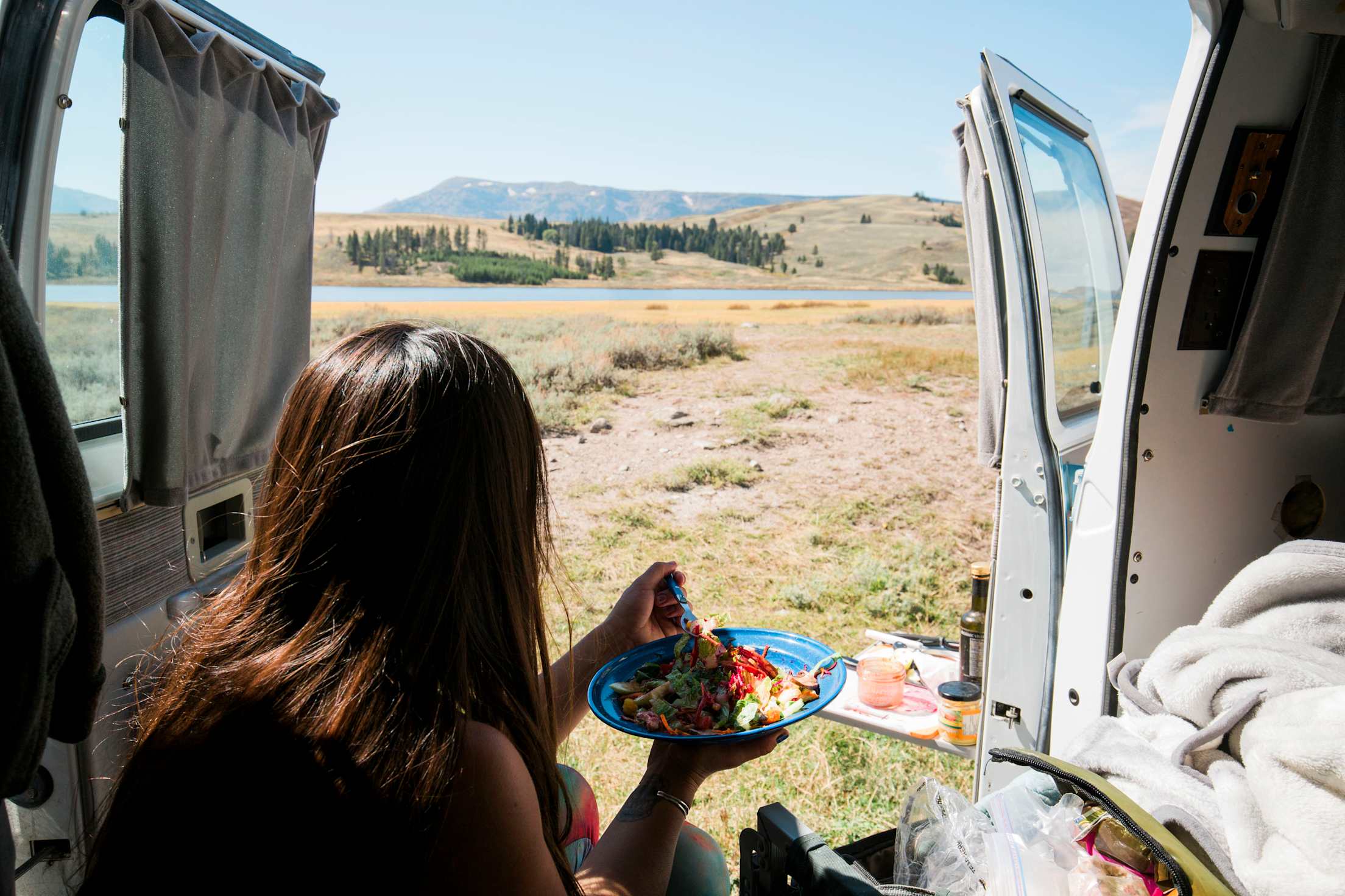 Picture of a woman eating lunch in a camper van looking towards mountains, picture