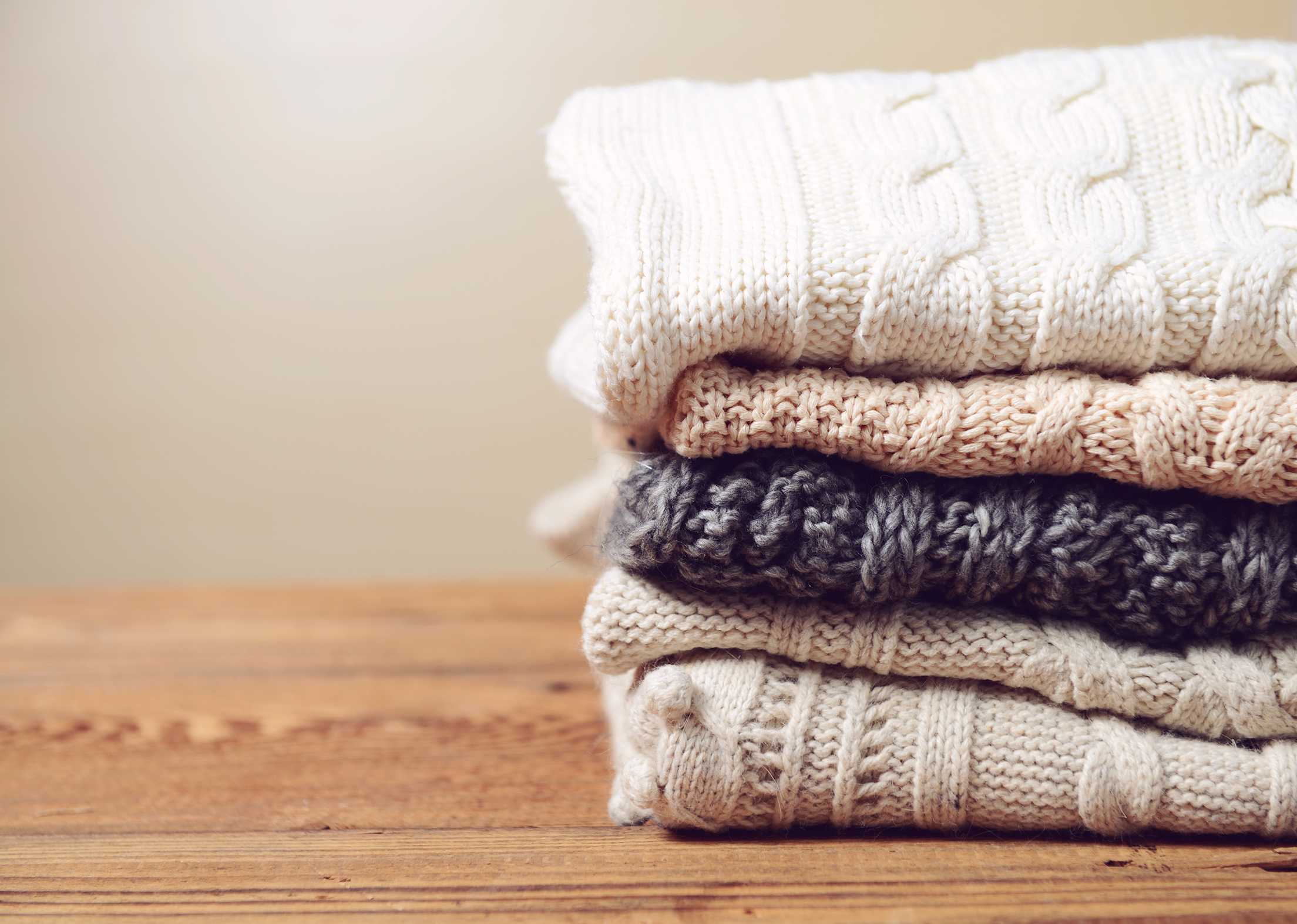 A stack of winter sweaters on a wood table, image