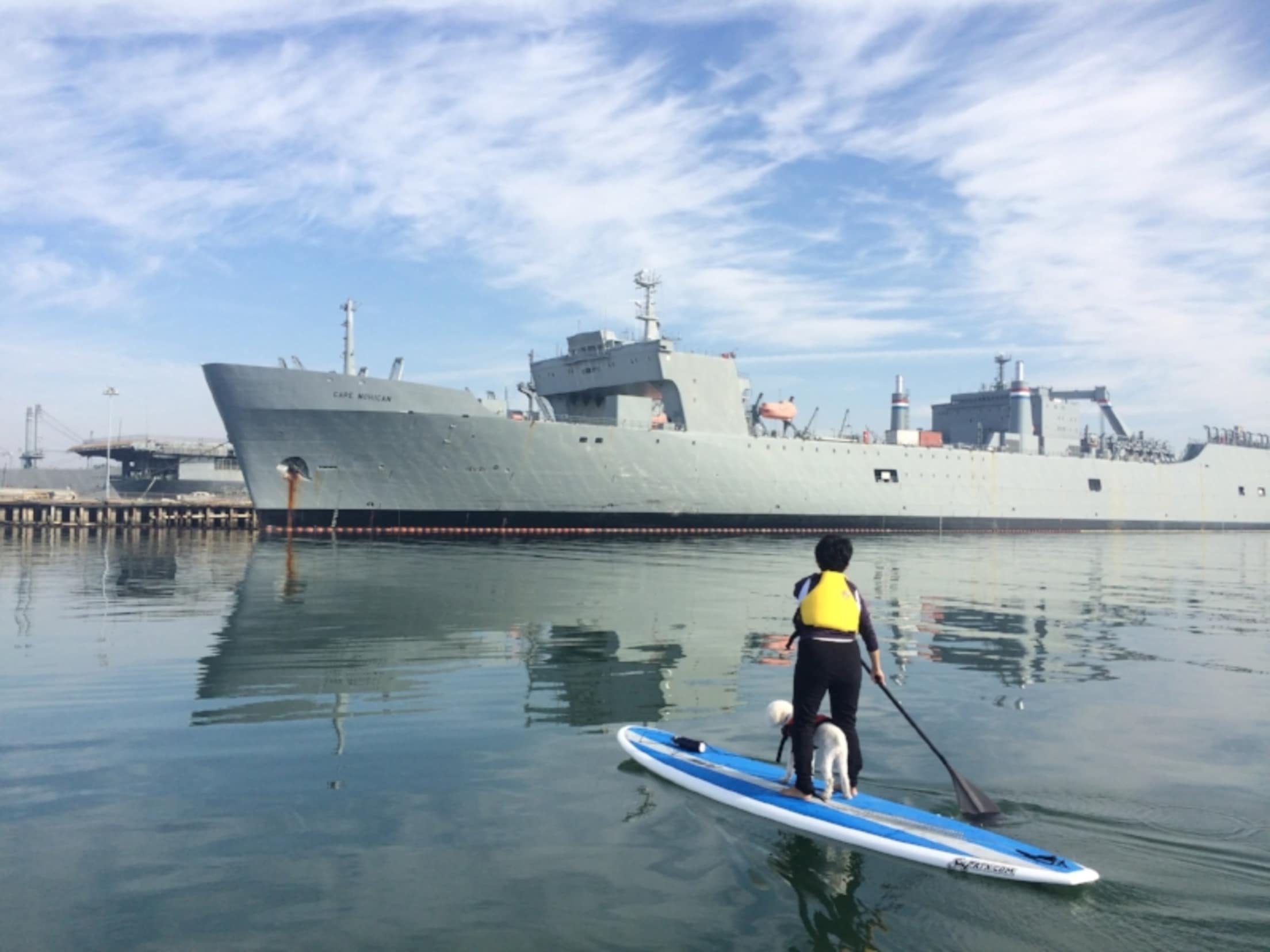 woman and dog on paddle board in front of USS Hornet in Alameda, CA, photo