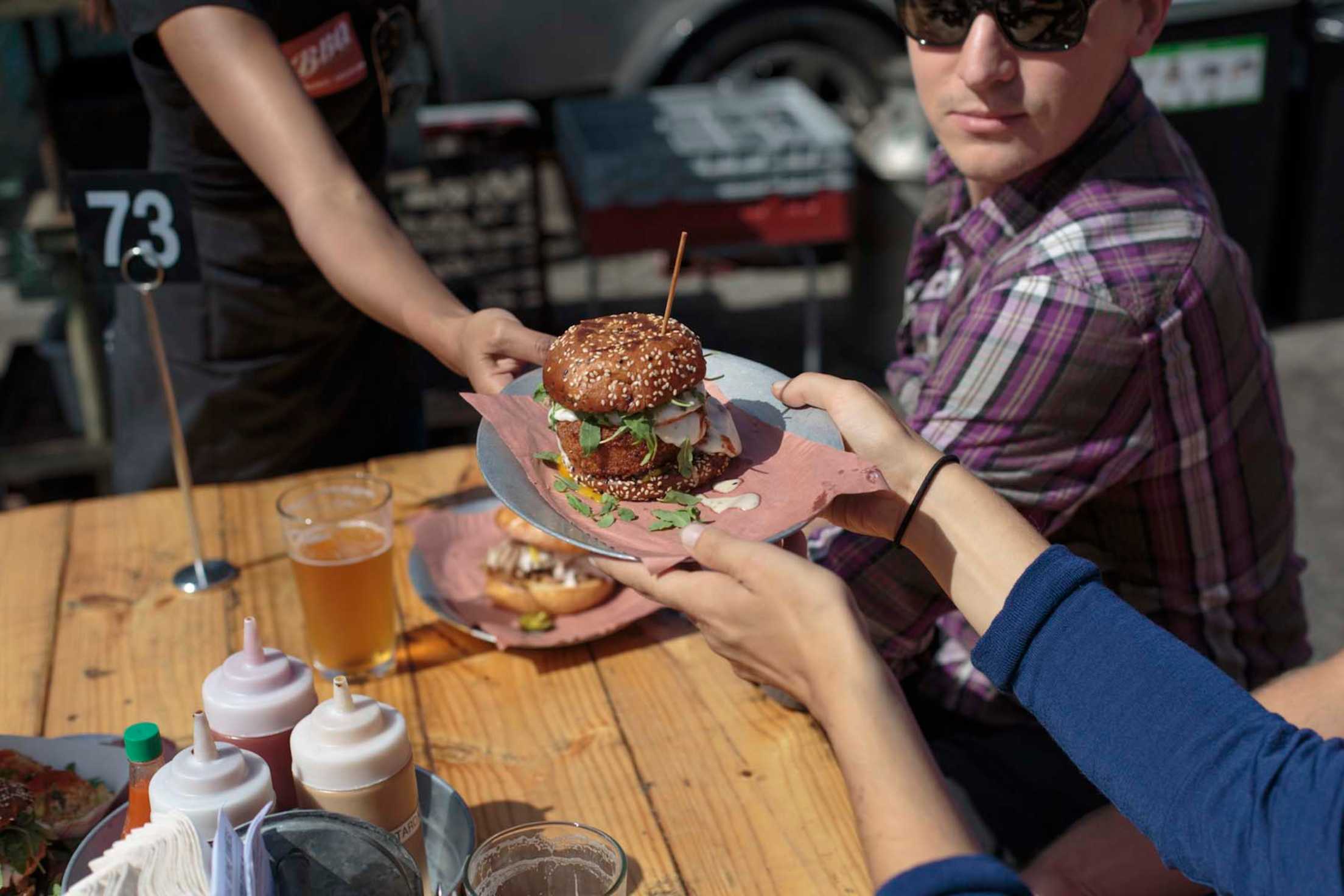 a diner takes a hefty sandwich at an outdoor table at 4505 Burgers & BBQ, San Francisco, picture