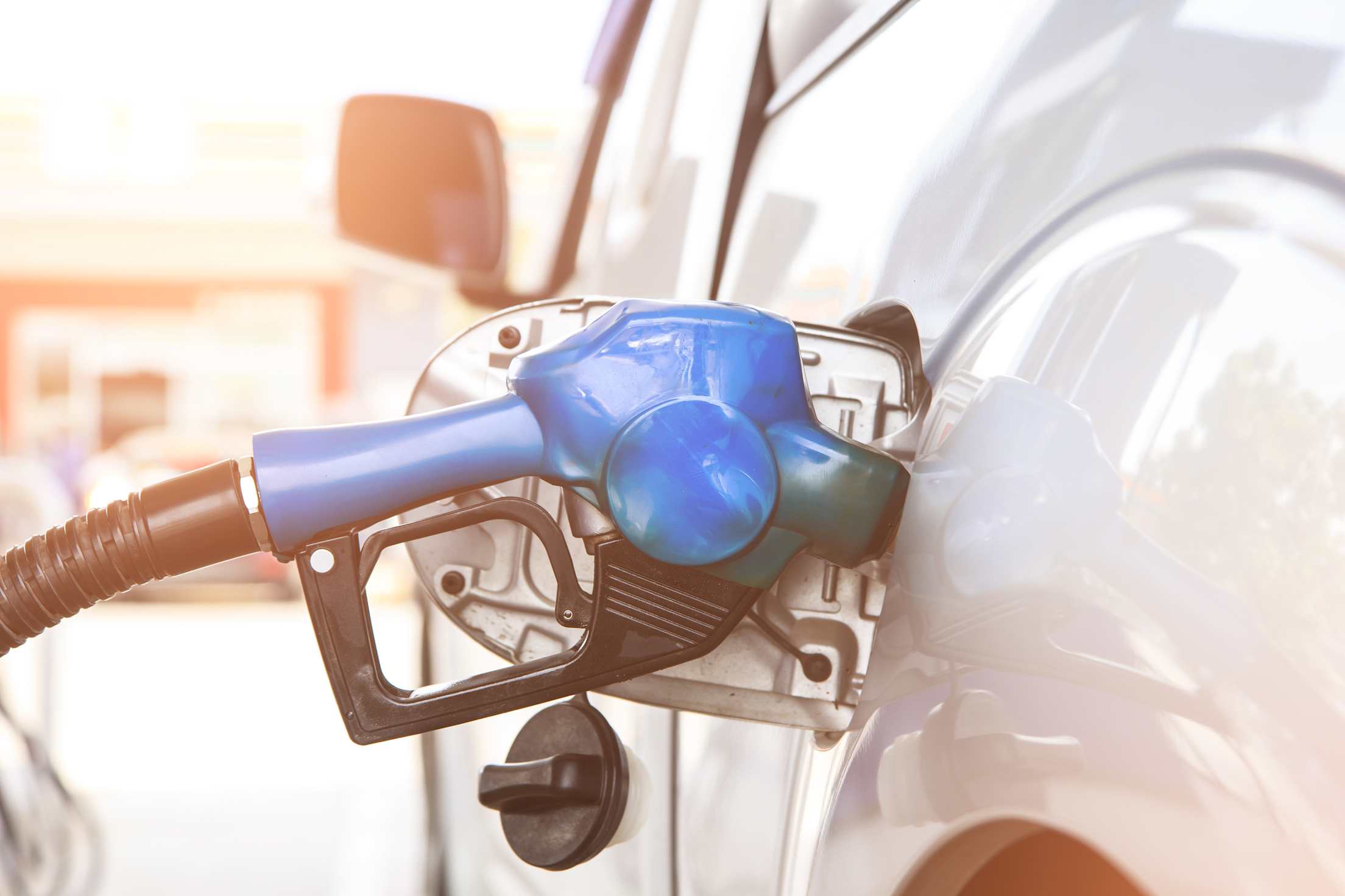 a blue fuel nozzle filling up gas tank on silver car at a gas station