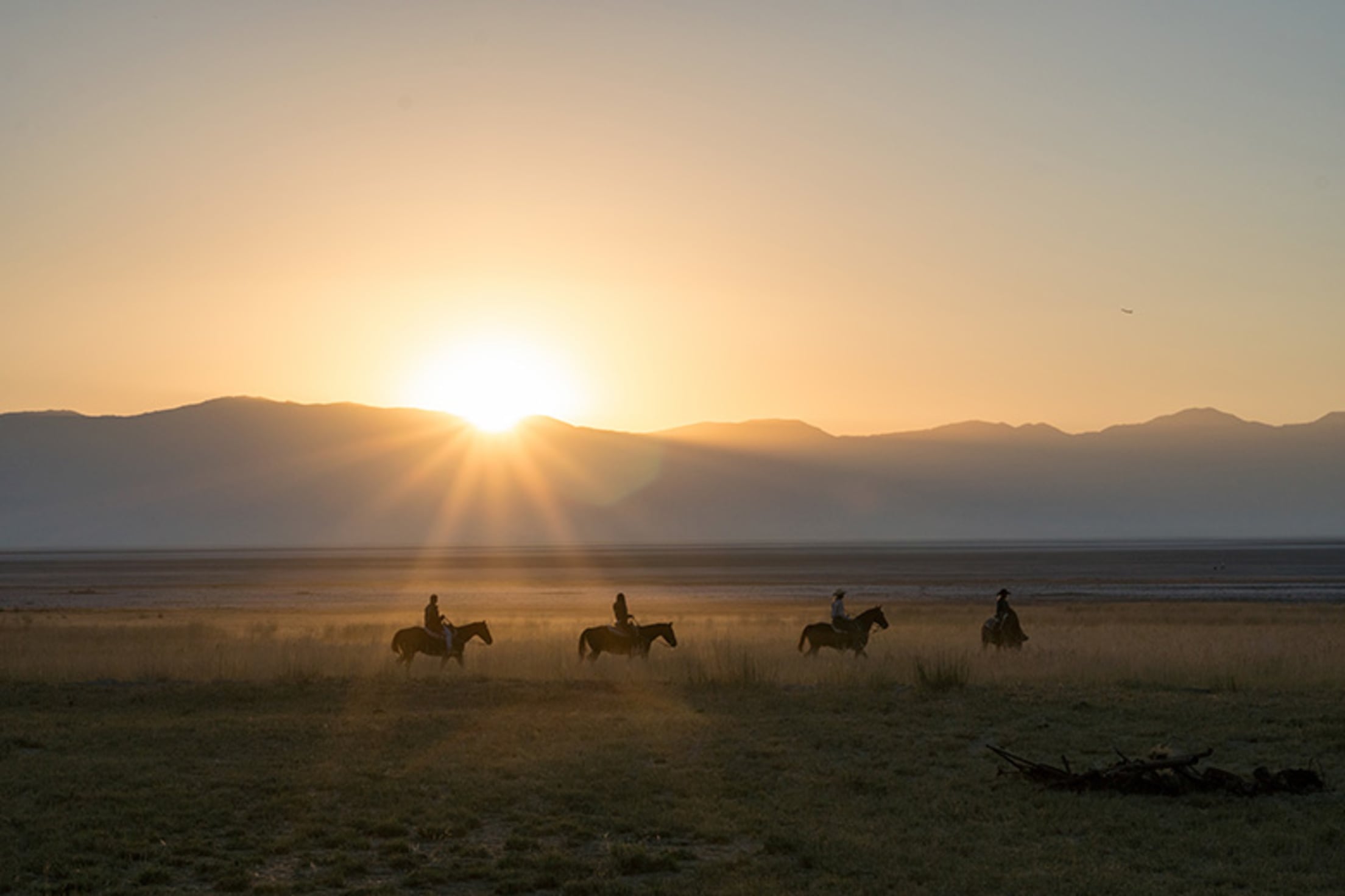 four riders on horseback tour follow a trail as sun peeks over mountains near Fielding Garr Ranch on Antelope Island in the Great Salt Lake, Utah, picture