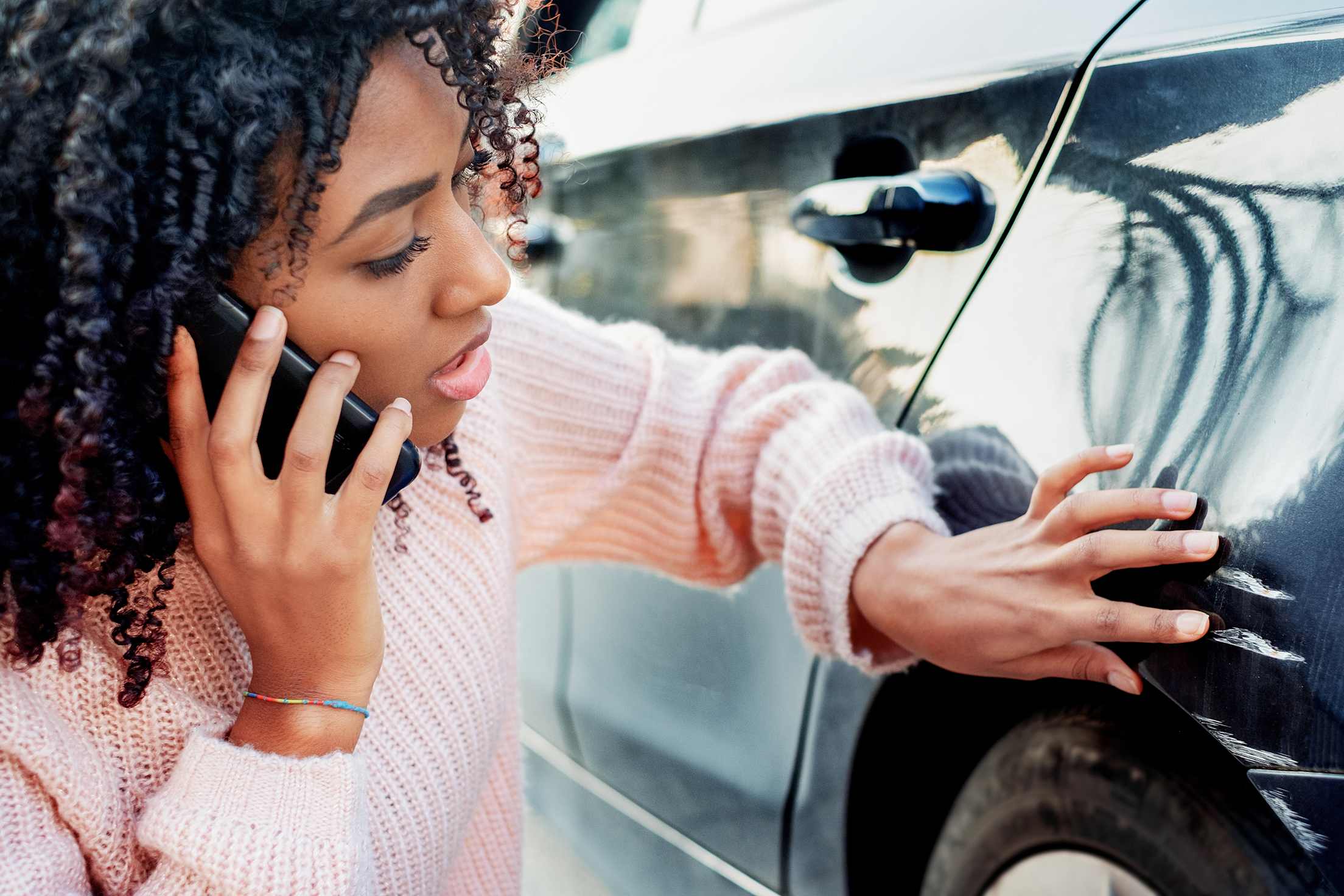 A driver inspects hit-and-run damage on her car.