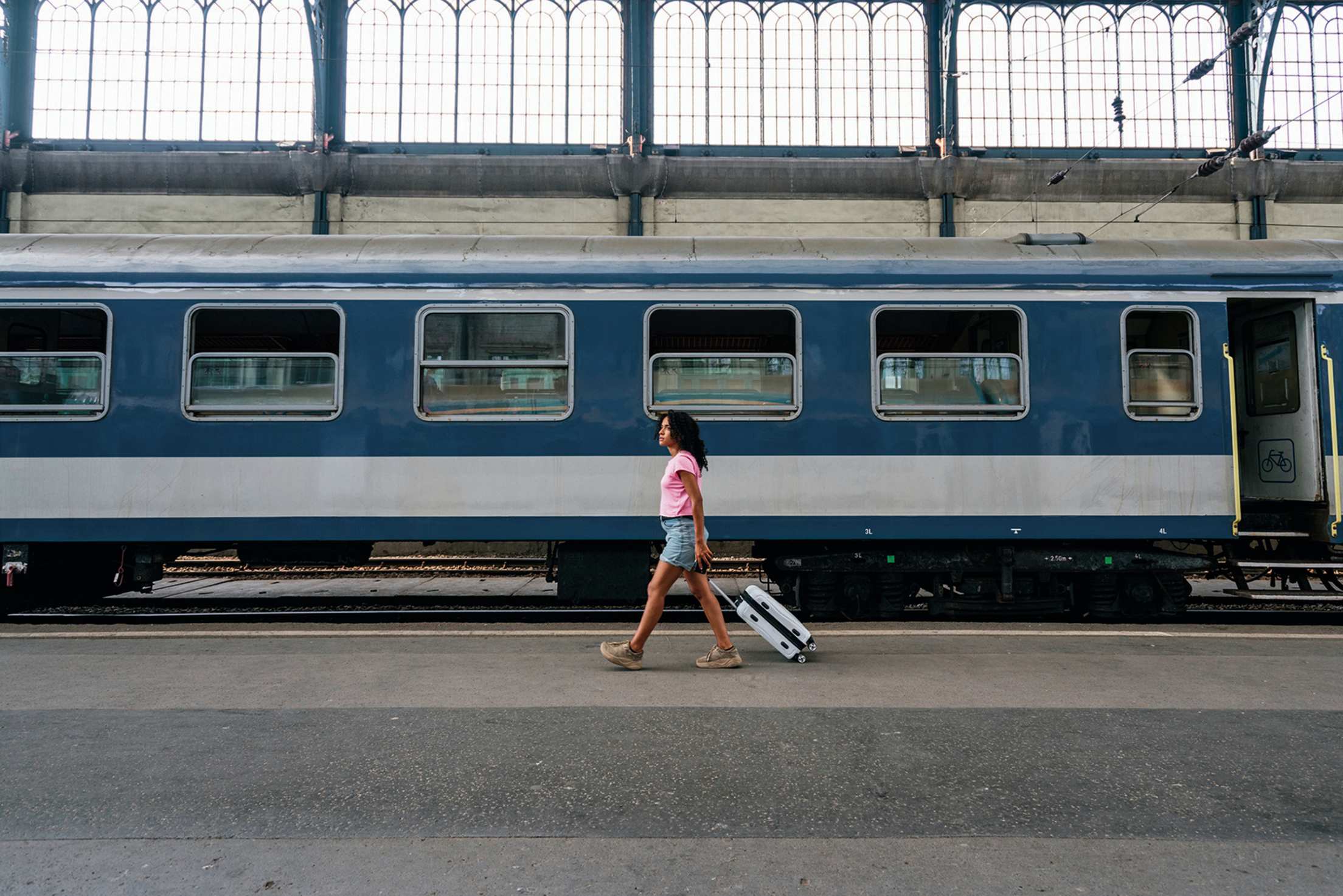 Woman walks past train cars while pulling suitcase in railway station