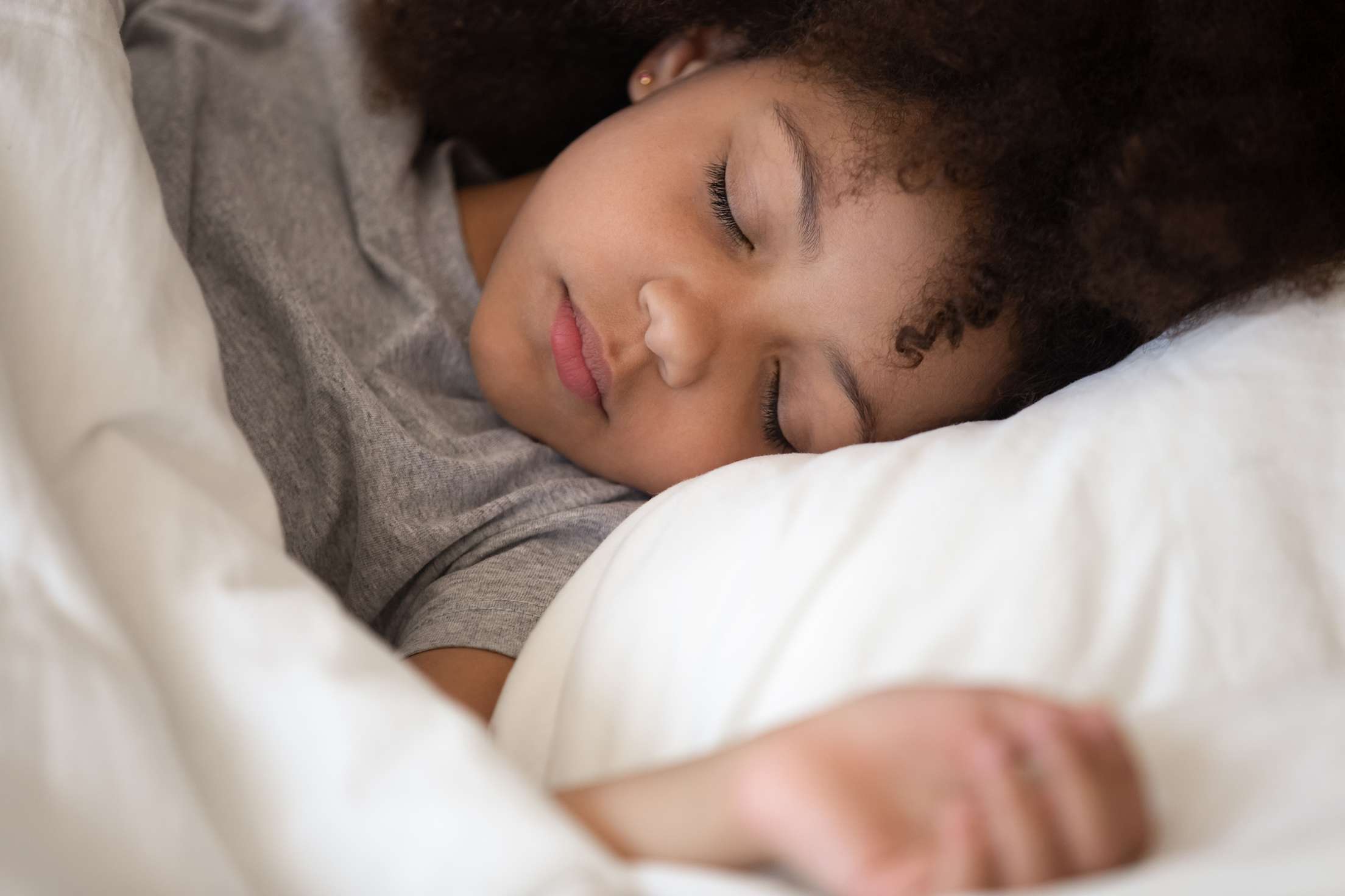A young child sleeping in white sheets.
