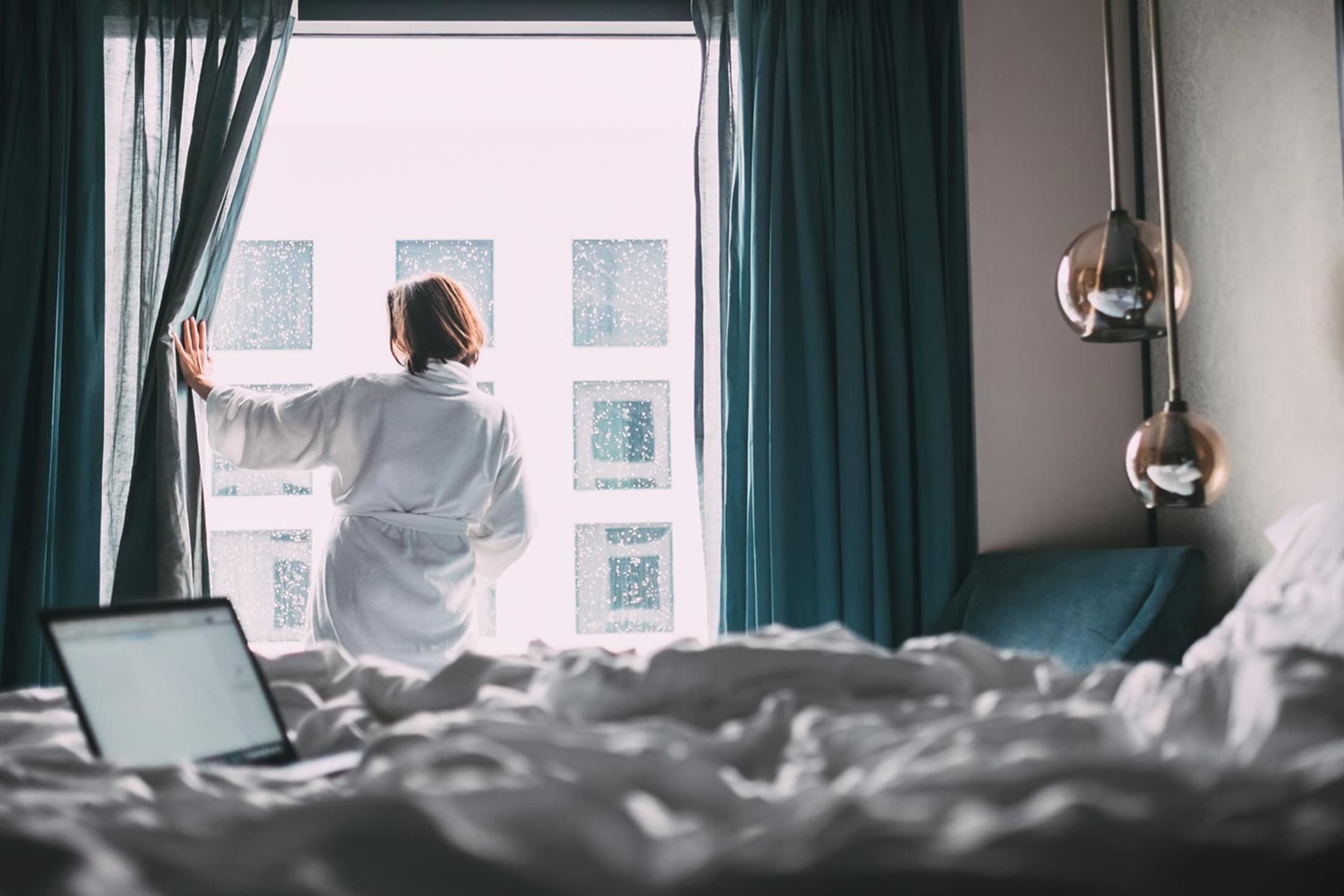 woman in white robe looking out hotel room window