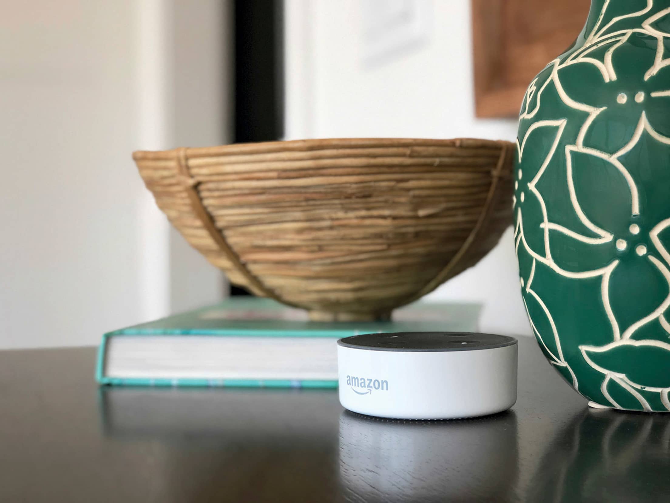 an Amazon Echo Dot smart home device sits on table by two ceramic bowls and book