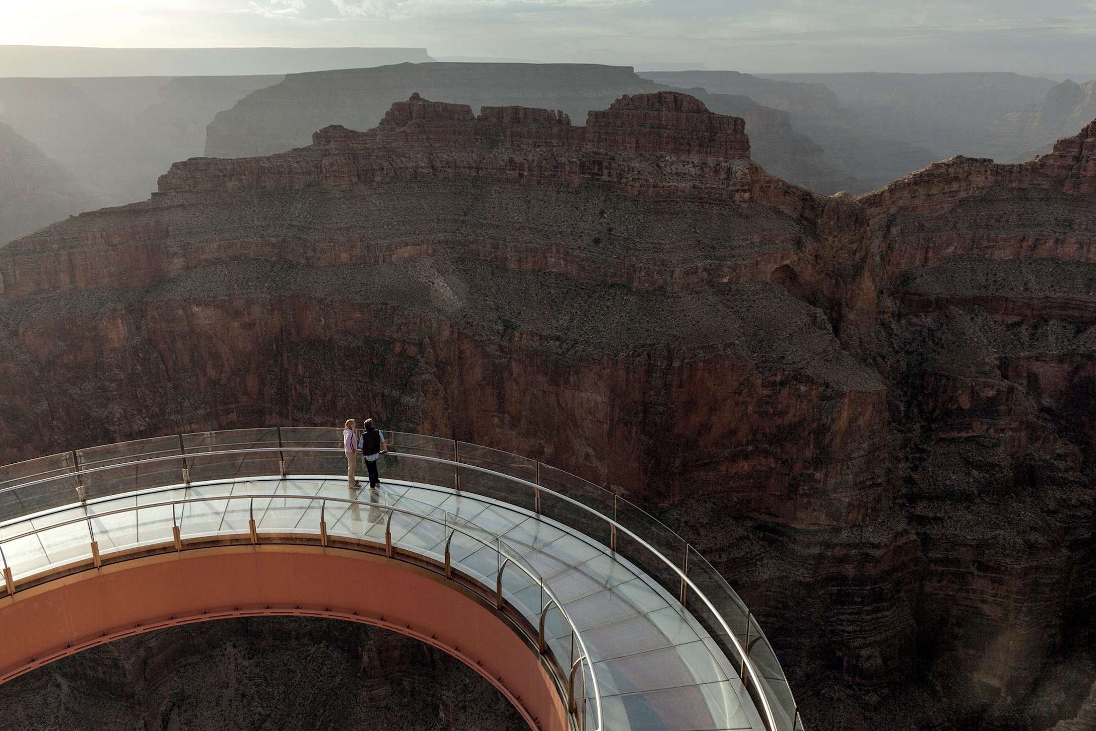 A pair of visitors take in the dramatic view from the horseshoe shaped Skywalk at Grand Canyon West