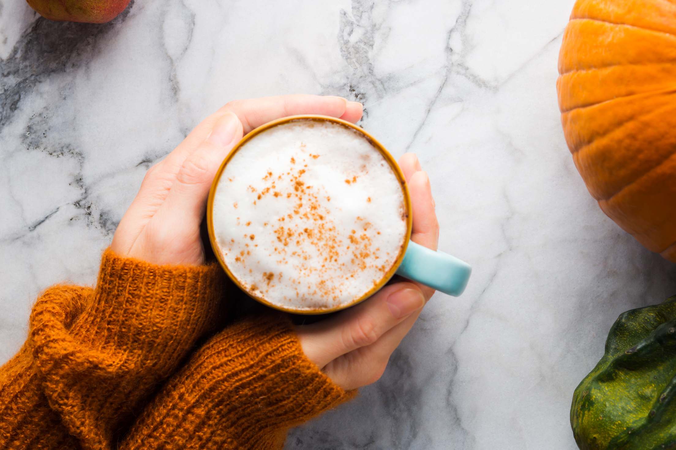 Hands hold a mug of homemade pumpkin spice latte.