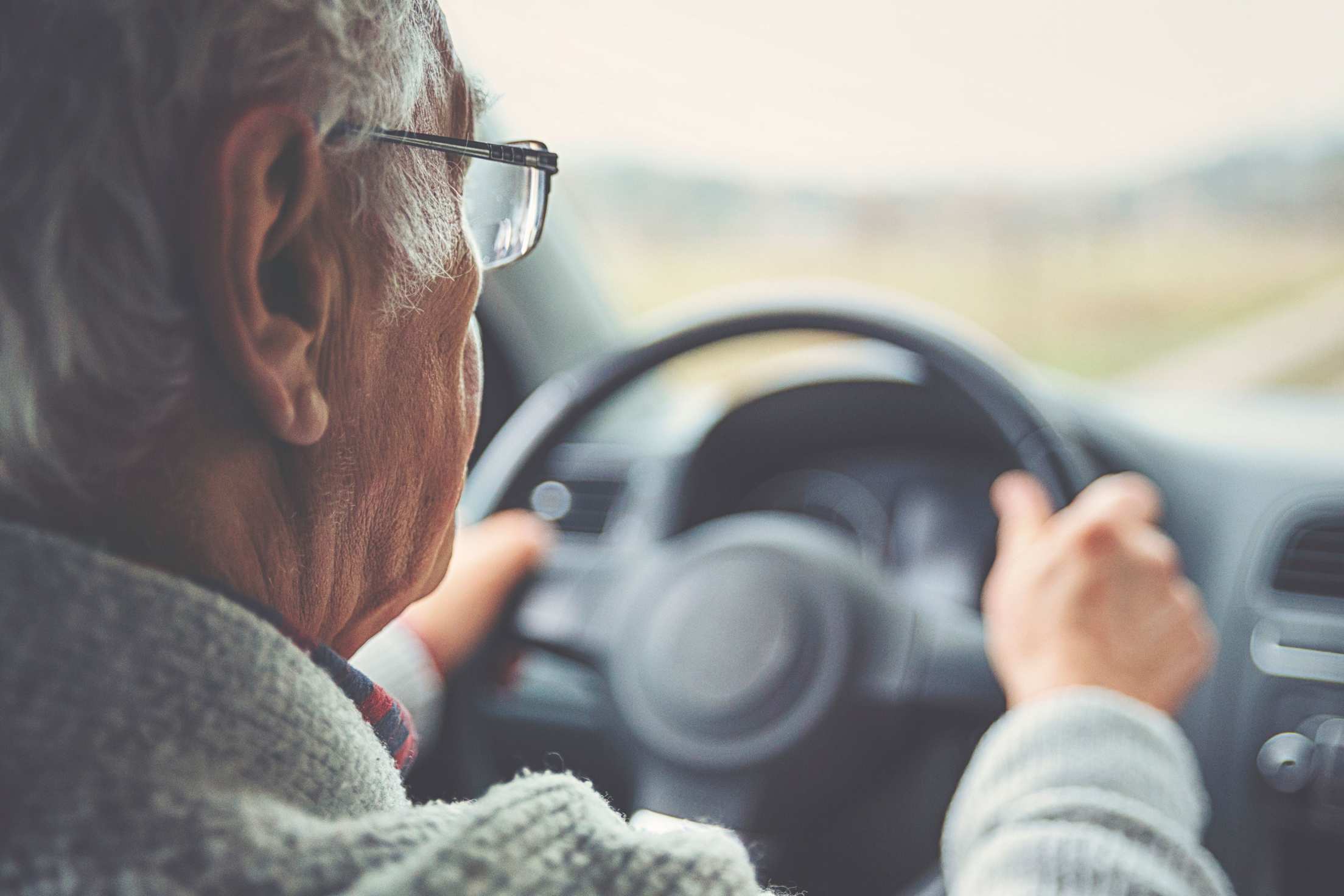 A senior man driving during the day with glasses on.