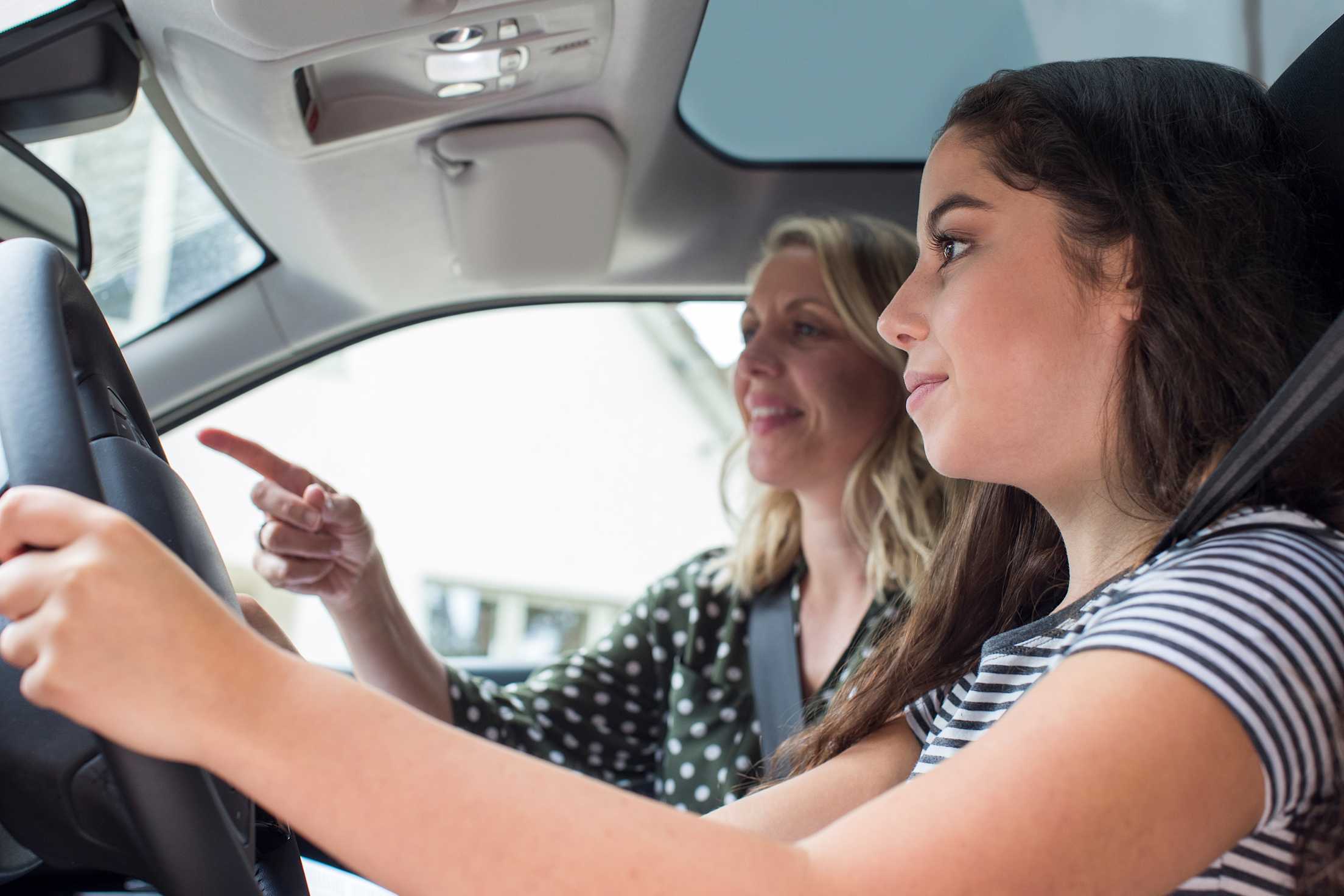 A teen practices driving with her mom.
