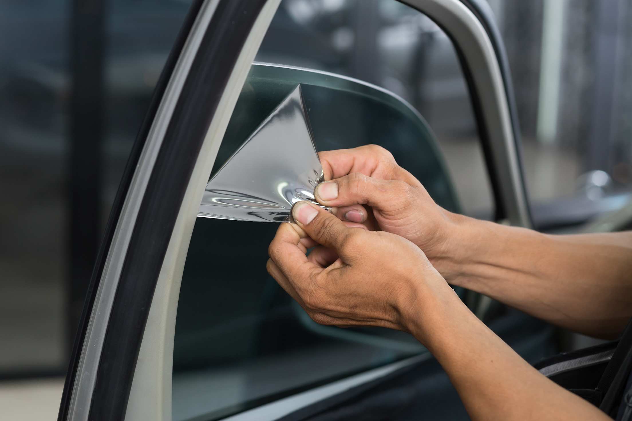 A person pulls window tinting film off their driver's side window.