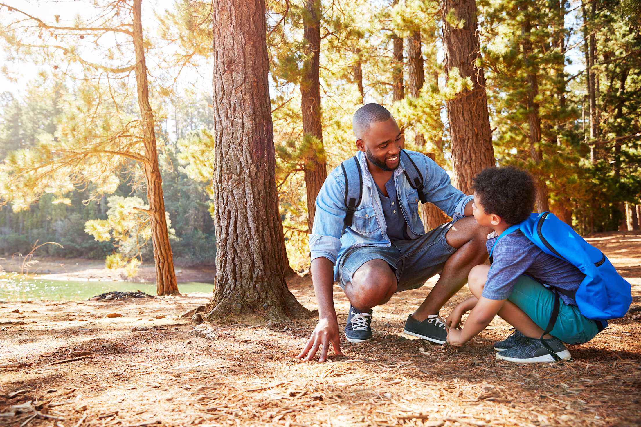 A father and son look for animal tracks on a dirt hiking trail.